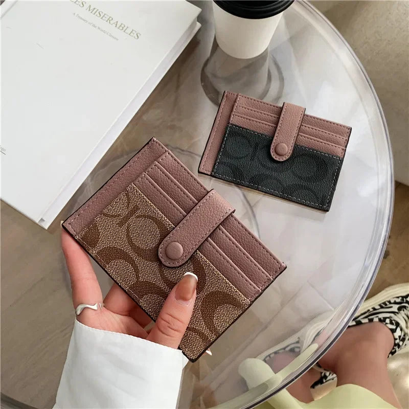Une main tient un porte-cartes en cuir PU marron et fin avec une touche gris foncé sur une surface de verre transparent.