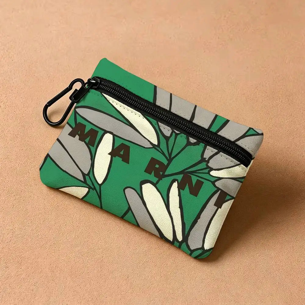 A green floral print mini coin purse with a zipper and carabiner clip resting on a beige surface.