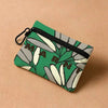 A green floral print mini coin purse with a zipper and carabiner clip resting on a beige surface.