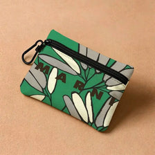 A green floral print mini coin purse with a zipper and carabiner clip resting on a beige surface.