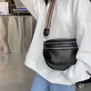 A person is holding a black soft leather crossbody bag with double zippers and an adjustable strap against a white jacket.