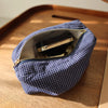 Pochette en tissu à carreaux bleu marine avec fermeture éclair dorée, contenant un produit cosmétique noir, posé sur une surf