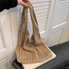A beige bohemian knit shoulder bag is being held by a hand, resting on a white surface.