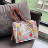 A clear plastic pouch with a floral pattern and red string ties is displayed on a dark sofa.
