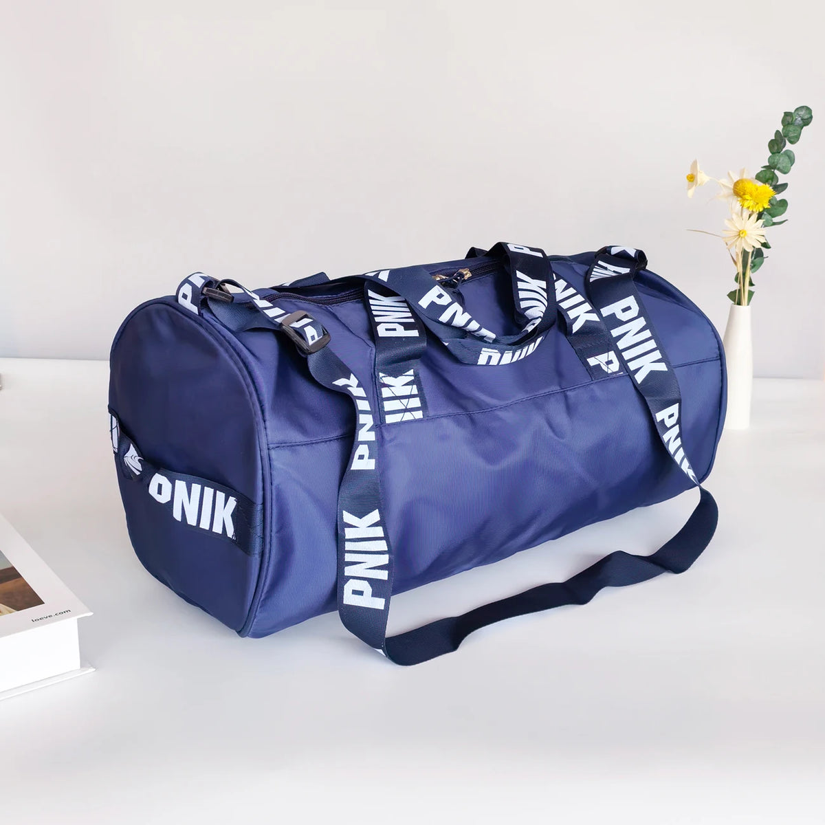 A navy blue Nike backpack with white text is displayed on a white surface next to a small vase of yellow flowers.