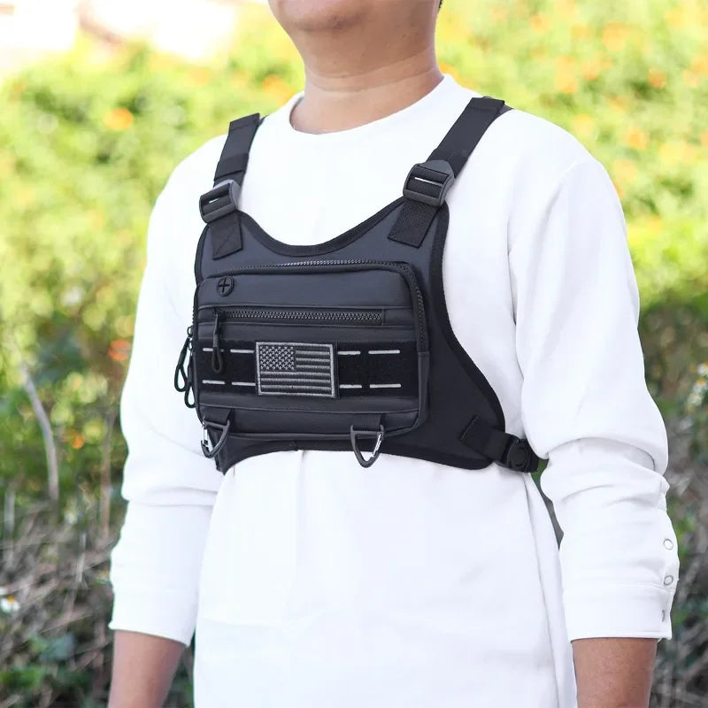 A black tactical chest bag with an American flag patch is worn on a white long-sleeved shirt.