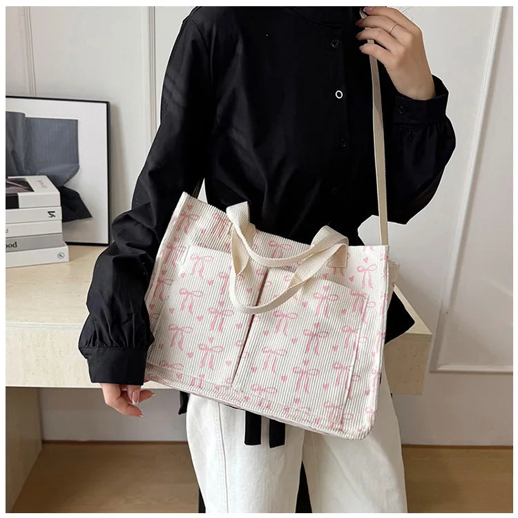 A woman holds a pink canvas tote bag with a white strawberry pattern against a light background.