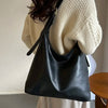 A black PU leather slouchy hobo shoulder bag carried by a person wearing a cream knit sweater.