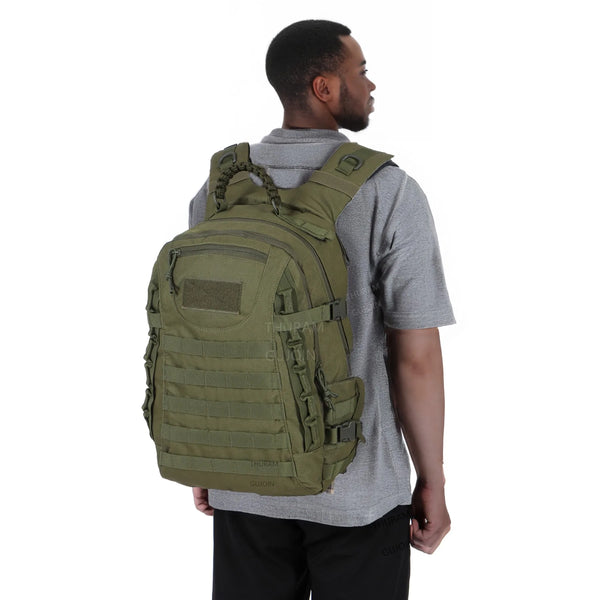 A man wearing a gray shirt is holding a tactical waterproof backpack.