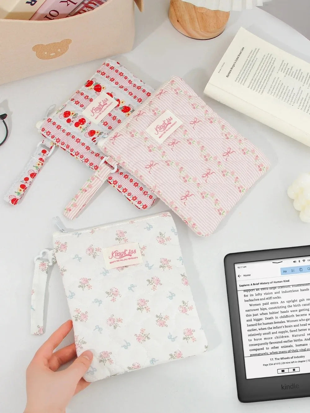 A light pink floral plaid cotton tablet pouch is shown next to a red patterned version and a wooden item on a white surface.