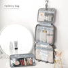 A gray toiletry bag with a hanging hook is displayed next to a circular mirror and some cosmetic products.