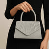 A woman holds a silver-grey pleated leather crossbody evening bag against a black dress.