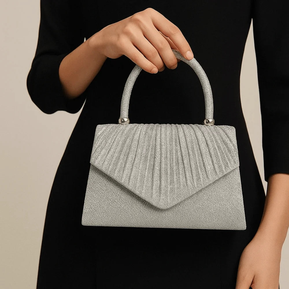 A woman holds a silver-grey pleated leather crossbody evening bag against a black dress.