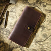 A brown genuine leather long bi-fold wallet with a snap closure resting on an old map.