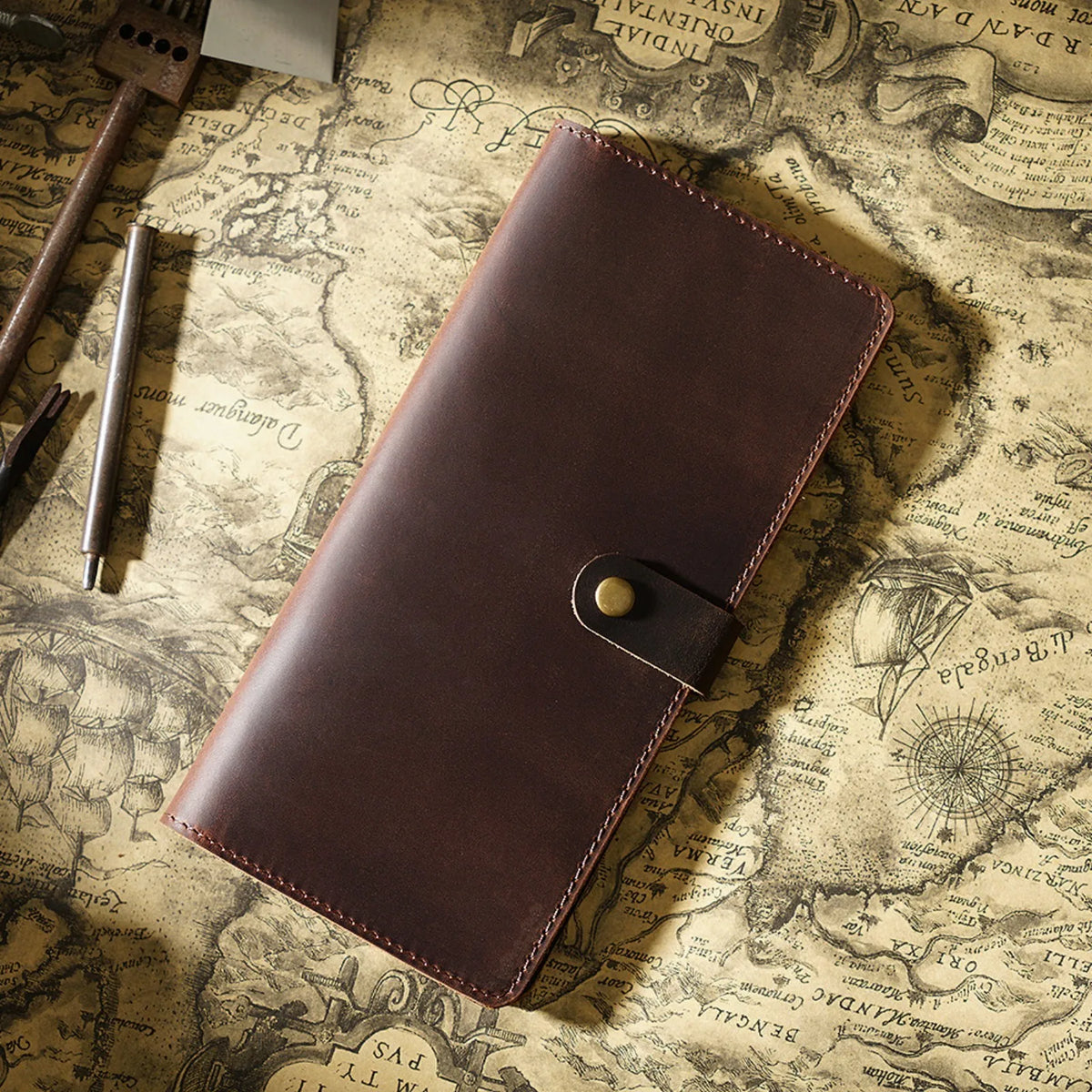 A brown genuine leather long bi-fold wallet with a snap closure resting on an old map.