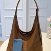 A brown PU leather slouchy hobo shoulder bag resting on a white surface next to a smartphone.