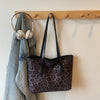 A dark gray leopard print vintage tote bag is hanging on a wooden shelf next to a pair of silver headphones.