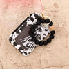 A black and white cow print card holder wallet with a gold tassel keychain and black beads on a light background.