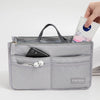 A gray fabric organizer pouch holds a smartphone and earbuds, with a hand inserting a small packet into the top.