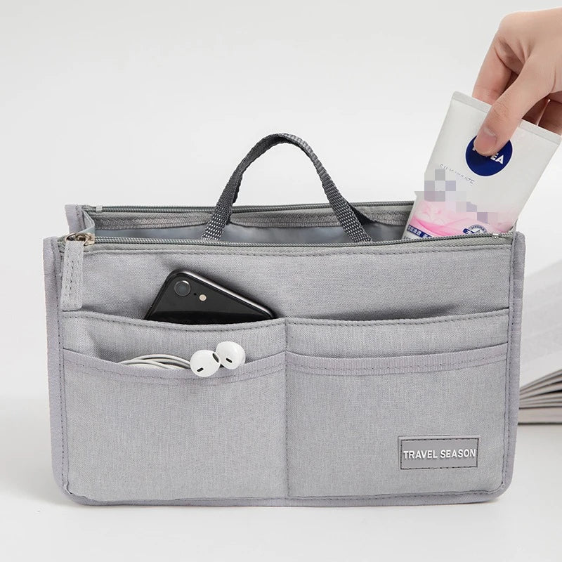 A gray fabric organizer pouch holds a smartphone and earbuds, with a hand inserting a small packet into the top.
