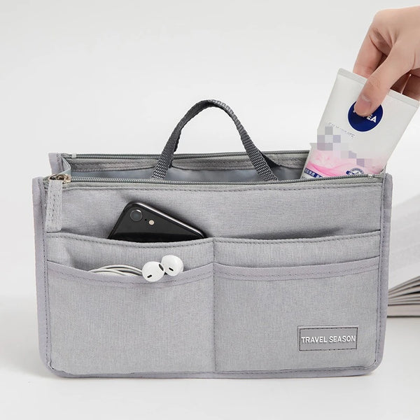 A gray fabric organizer pouch holds a smartphone and earbuds, with a hand inserting a small packet into the top.