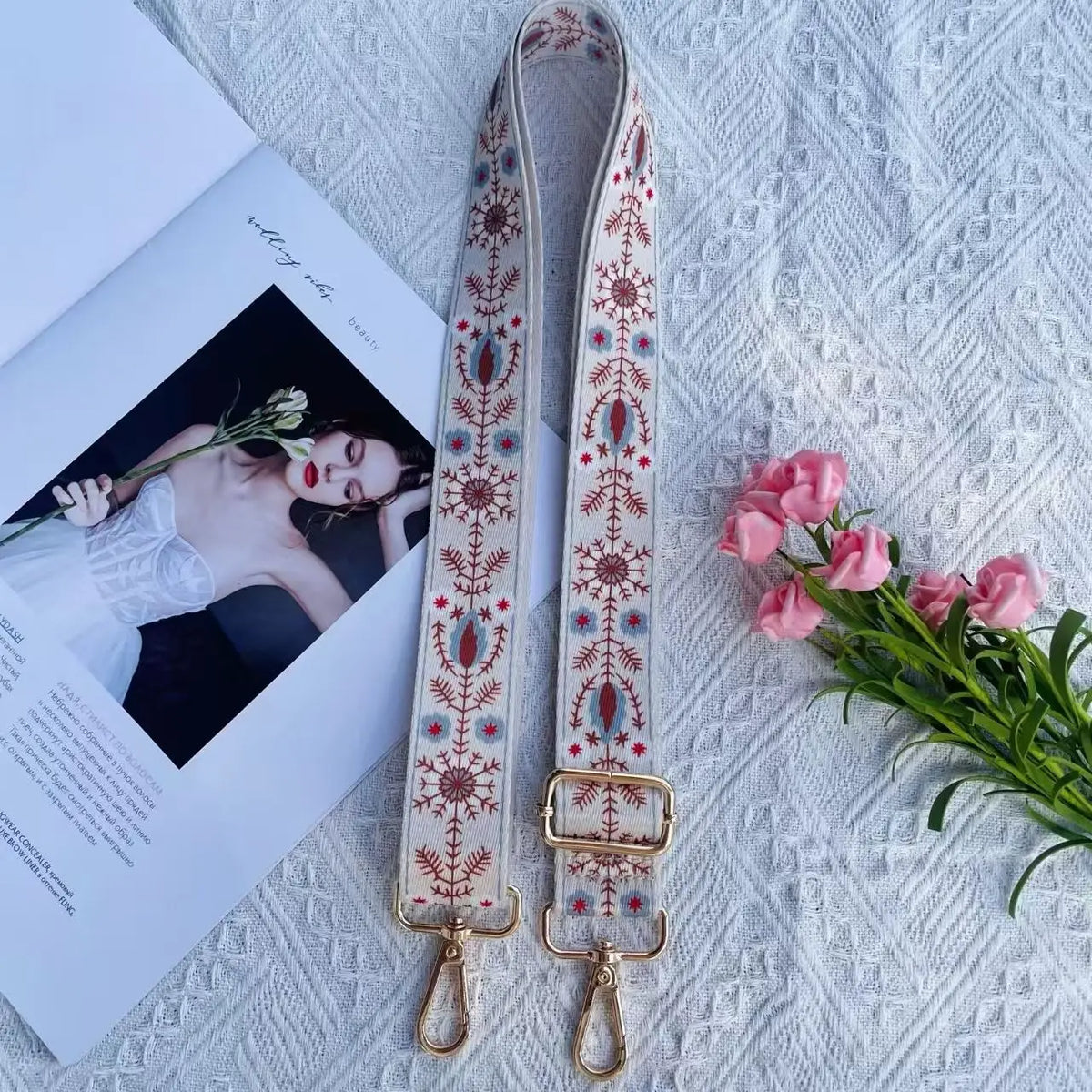 A close-up of a beige and red patterned nylon bag strap with gold hardware resting on a white textured surface.