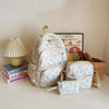 A set of cute bow print nylon travel backpacks displayed on a white surface next to a framed picture and a potted plant.