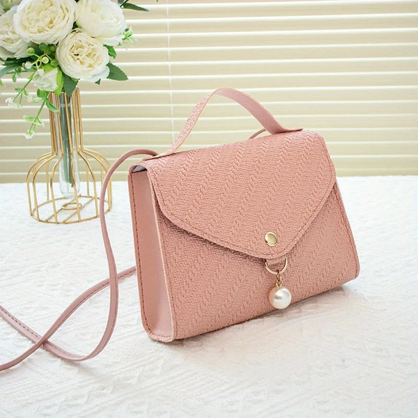 A light pink beaded square crossbody bag with a gold-tone chain and adjustable strap resting on a white surface.