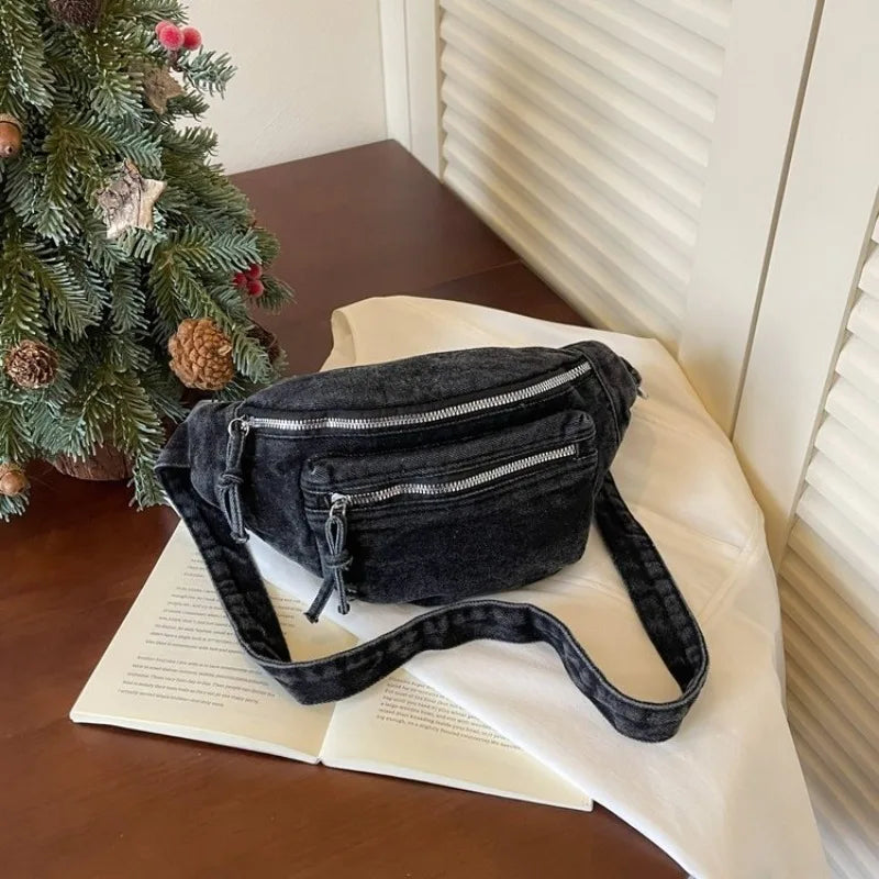 Sac bandoulière en denim vintage gris foncé posé sur un tissu blanc à côté d'un sapin de Noël.
