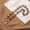 A gold-toned acrylic handbag strap chain laid across a piece of paper on brown fabric.