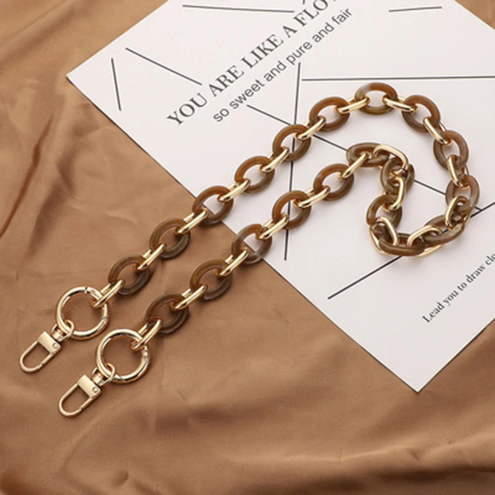 A gold-toned acrylic handbag strap chain laid across a piece of paper on brown fabric.