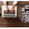 A laptop is open on a wooden table with hands typing, next to a leather cable storage organizer bag.