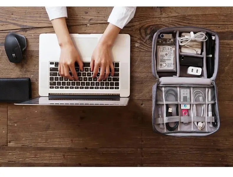 A laptop is open on a wooden table with hands typing, next to a leather cable storage organizer bag.