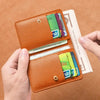 A brown PU leather small wallet is shown open, displaying various cards and cash next to a banknote.