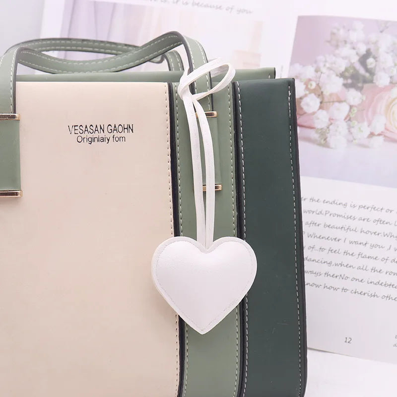 A light beige leather pouch with a white heart charm and dark green leather straps.