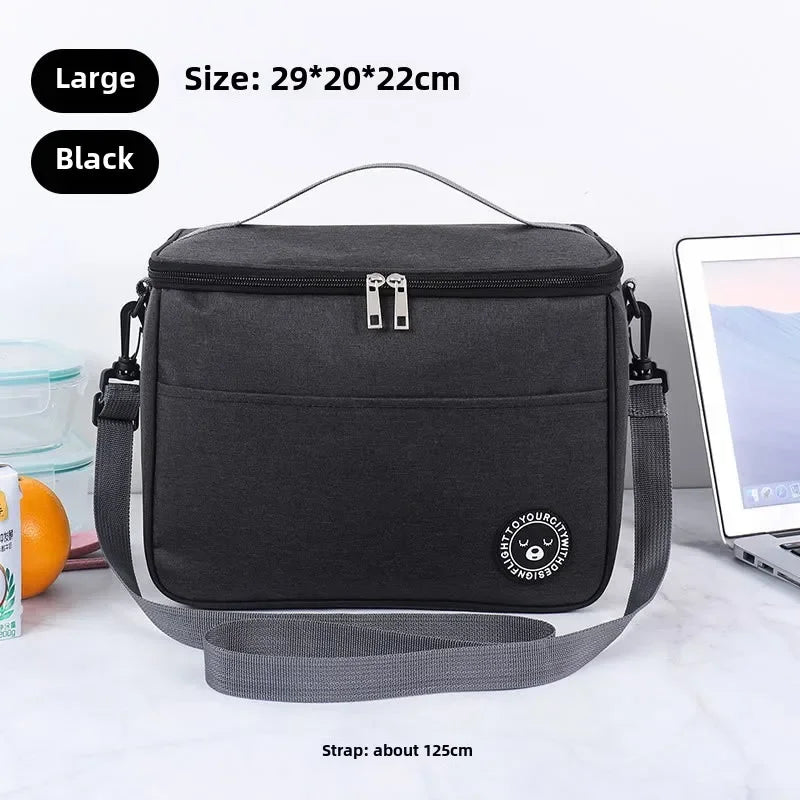 A black insulated portable lunch bag with a shoulder strap is shown on a white surface.