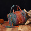 A luxury crocodile pattern crossbody tote bag in green and brown leather resting on a wooden surface next to a piece of drift