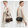 A woman models a beige blazer and white skirt while carrying a black leather shoulder bag with gold hardware.