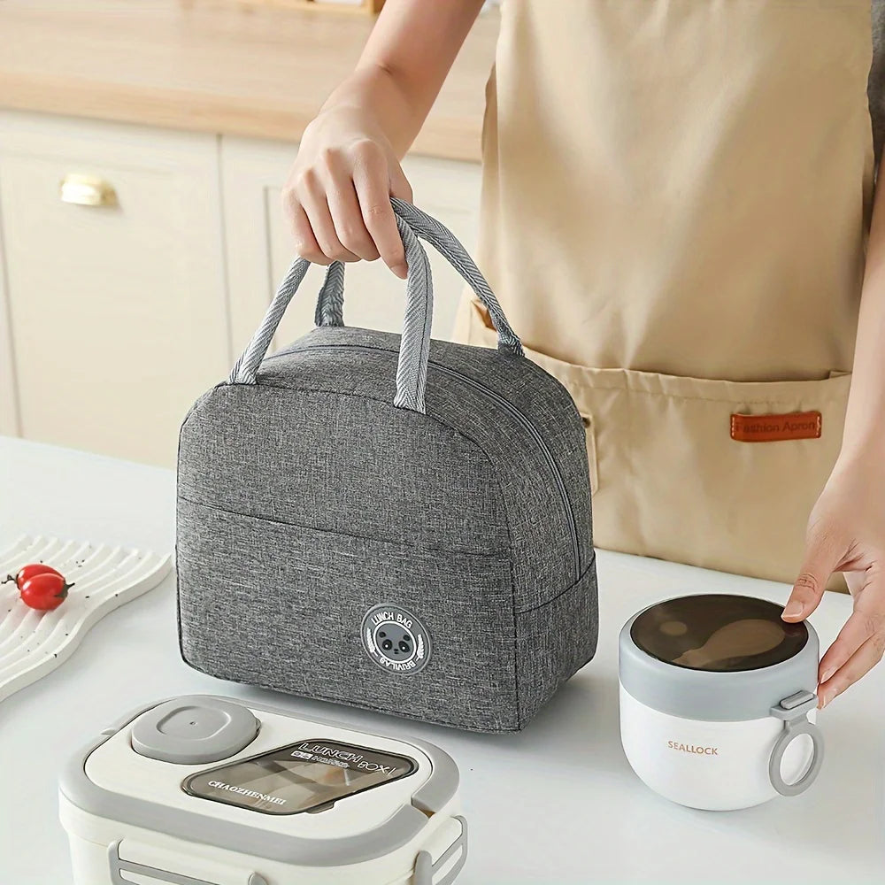 A person holds a gray insulated lunch bag next to a ceramic mug and a white food container on a table.