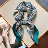 A silk paisley scarf tied in a bow, featuring teal and white patterns, displayed on a light background.