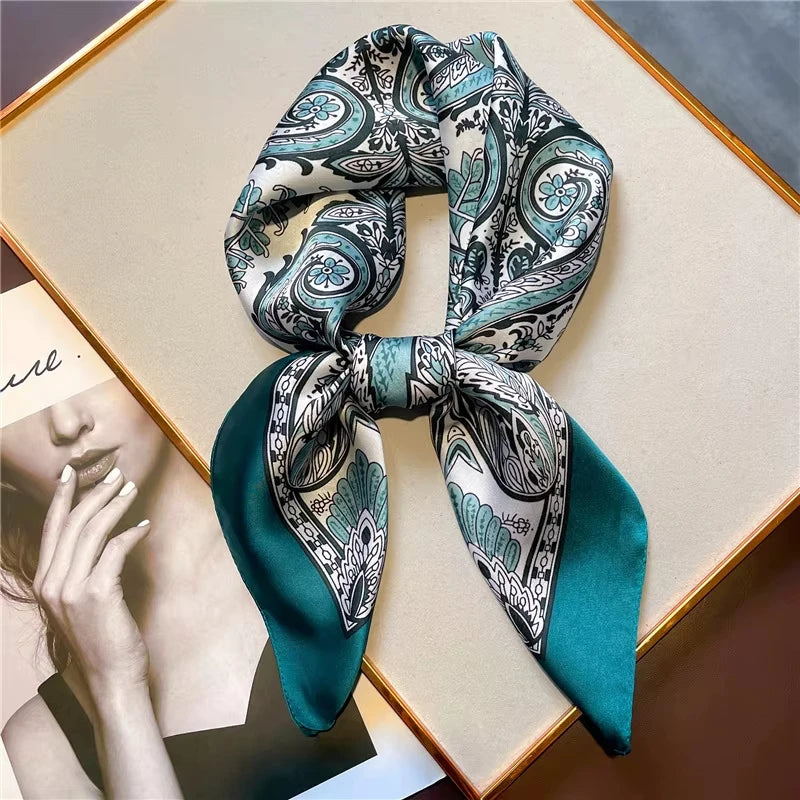 A silk paisley scarf tied in a bow, featuring teal and white patterns, displayed on a light background.