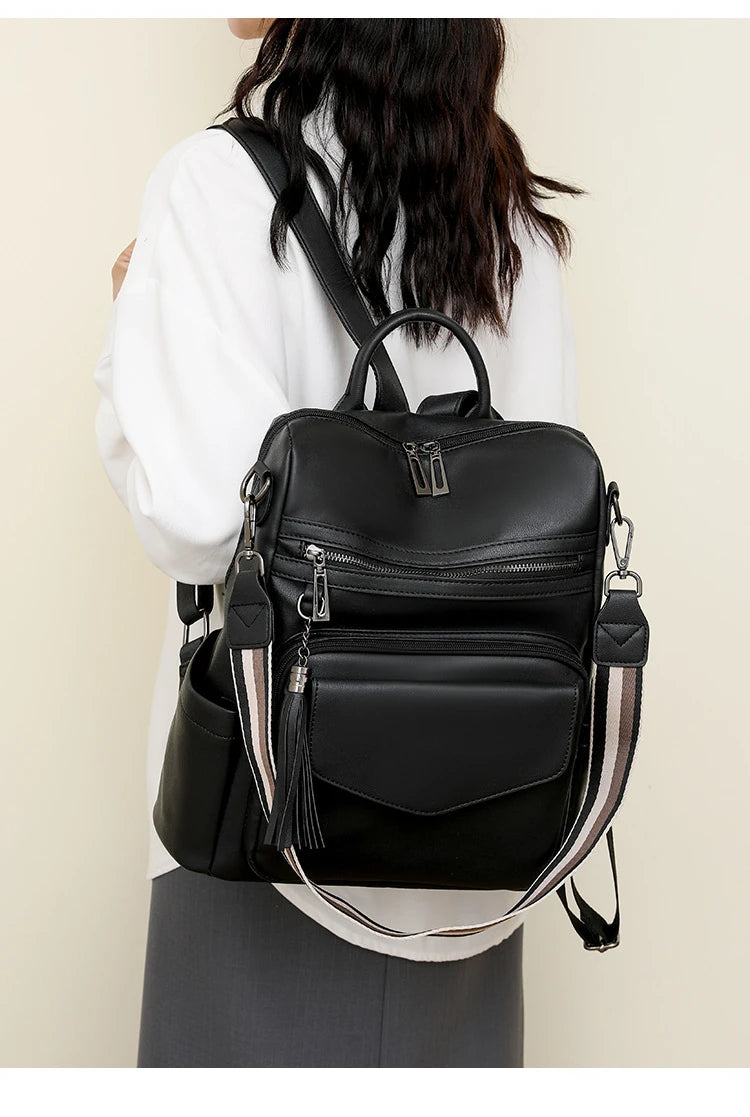 A woman is holding a black retro PU leather travel backpack with tassel details.
