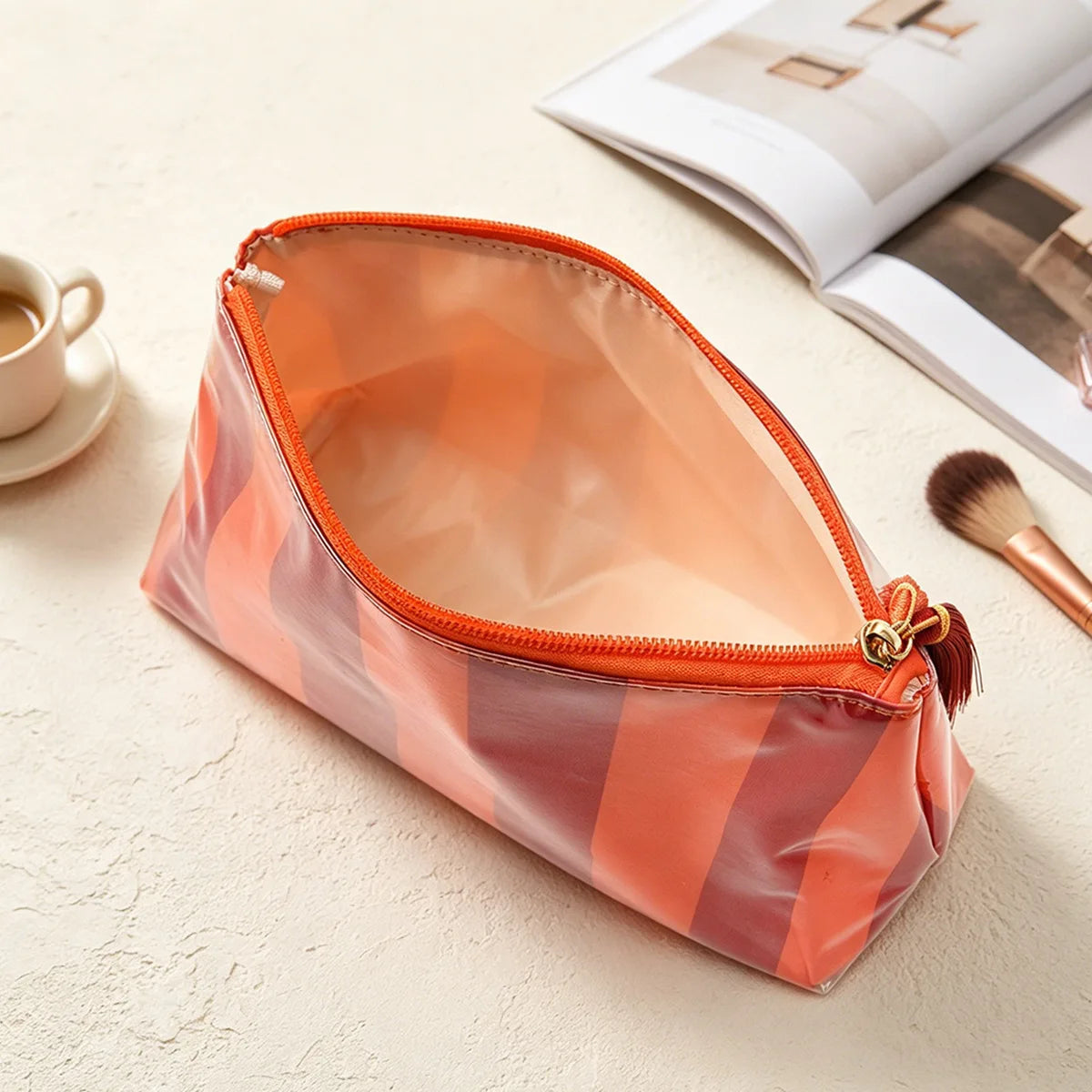 An open, striped orange cosmetic travel pouch with a fringe detail resting on a light surface.