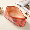 An open, striped orange cosmetic travel pouch with a fringe detail resting on a light surface.