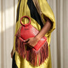 A hand holds a red fringed clutch bag with tassels against a yellow and black draped garment.