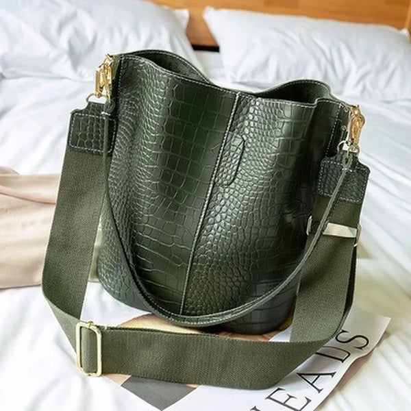 A dark olive green vintage alligator pattern leather crossbody bag resting on white bedding.