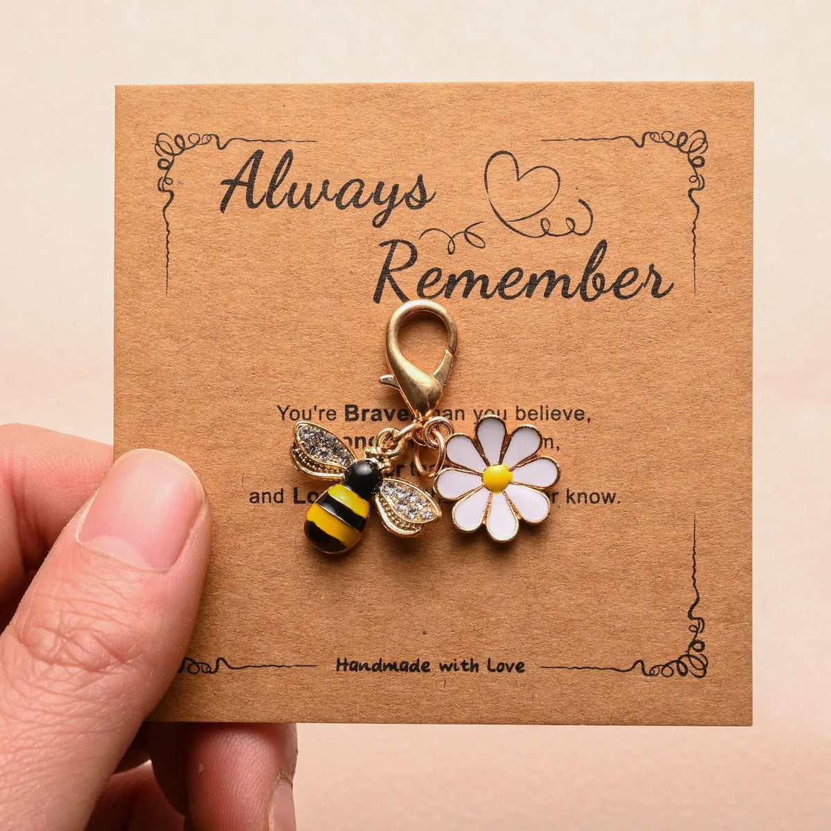 A handmade brown card featuring a gold-colored bee and flower keychain, with text that reads Always Remember.