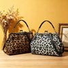 A faux leather leopard print handbag with a top handle and crossbody strap resting on a wooden surface against a yellow backg