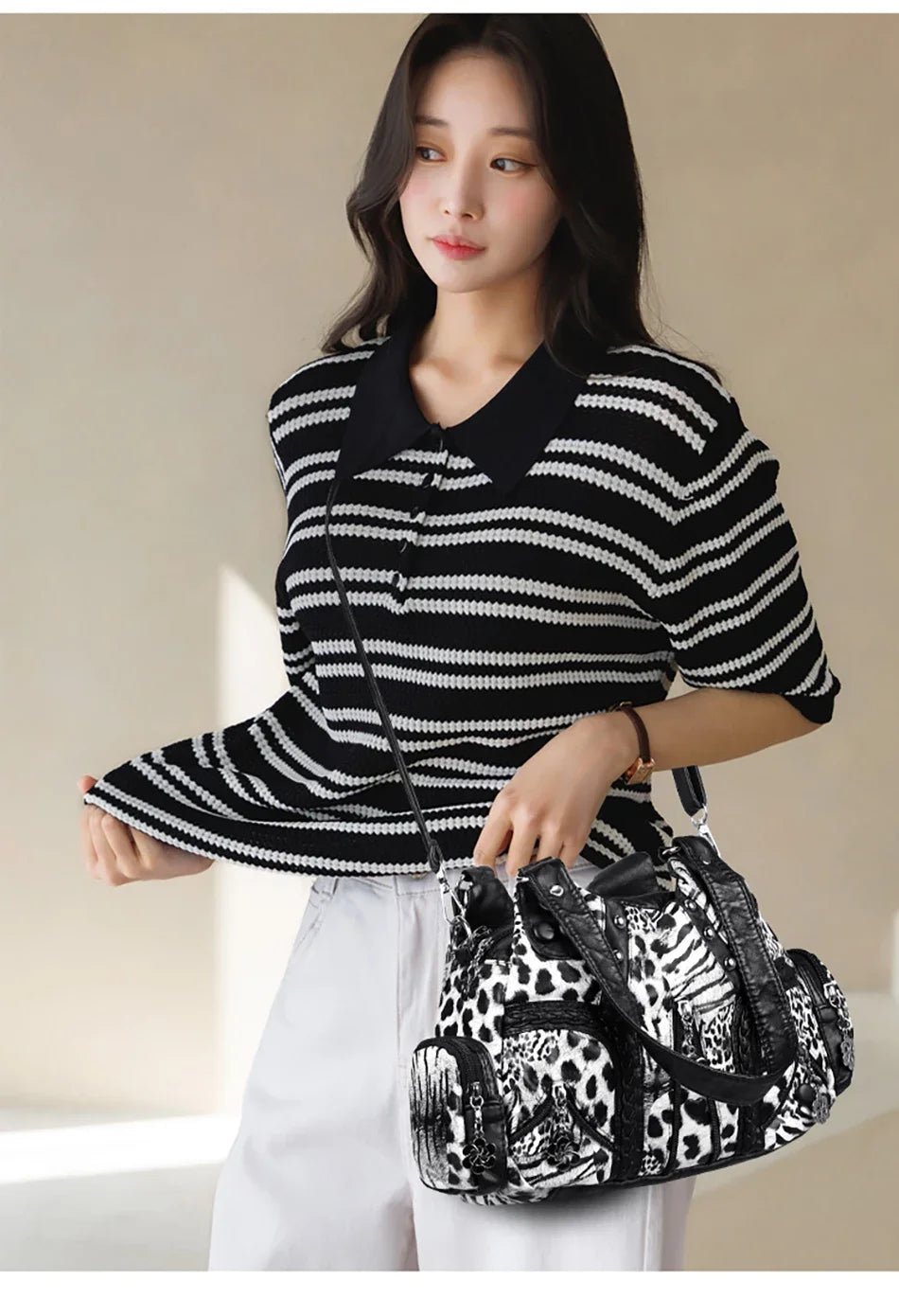 A woman models a black and white striped top and white pants while holding a spacious black leopard print PU leather tote bag