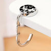 A silver zinc alloy folding handbag hook with a black and white spotted plate is displayed on a white surface.